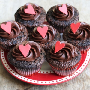 dark chocolate cupcakes with chocolate frosting and heart decor on red plate.