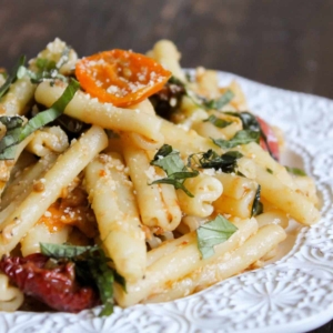 roasted tomato and pasta piled up on white plate.