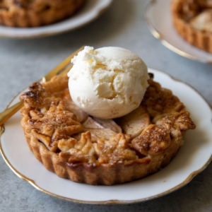 mini apple pie tart on serving plate with a scoop of vanilla ice cream.