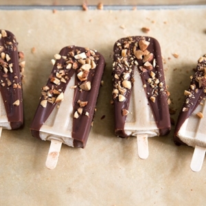 Banana Coconut Ice Pops with dipped in chocolate and almonds in a row on parchment paper.