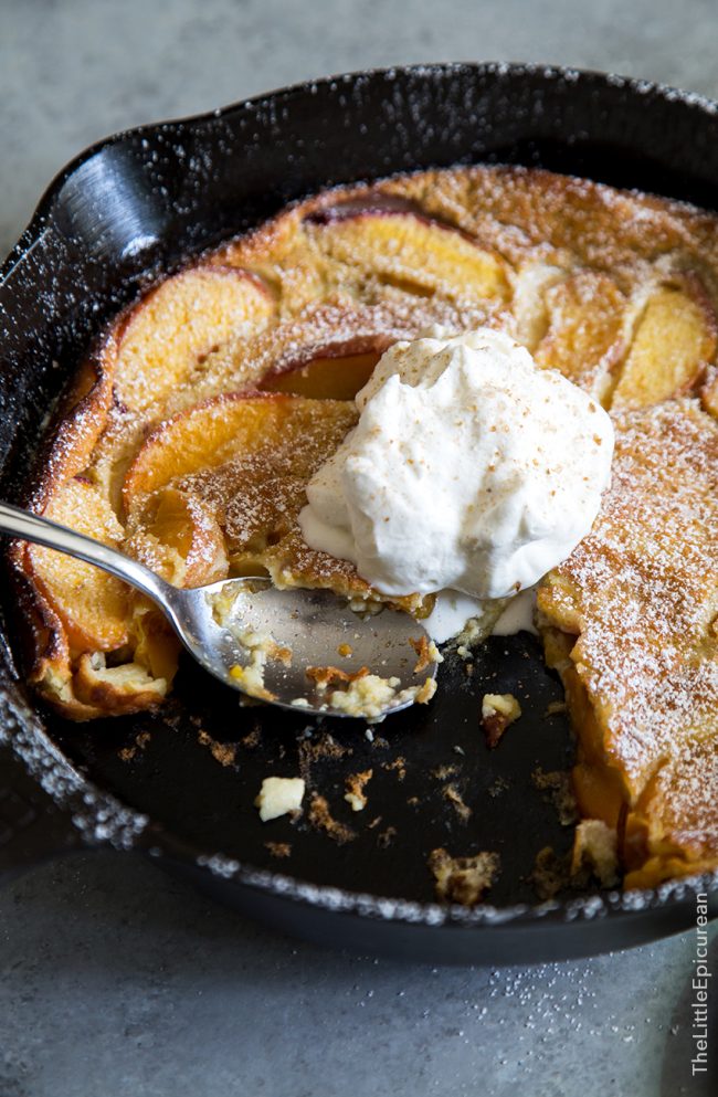 Whiskey peach clafoutis topped in whipped cream in cast iron skillet.