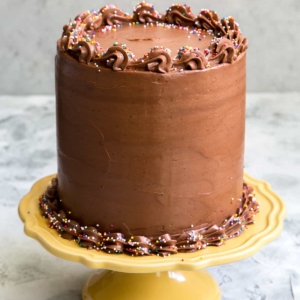 layered yellow cake coated in chocolate frosted and topped with sprinkles displayed on a yellow cake stand