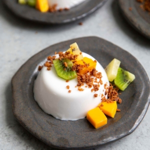 Coconut Panna Cotta served with latik and fresh fruits. Latik is from the Philippines. It is fried coconut milk curds.