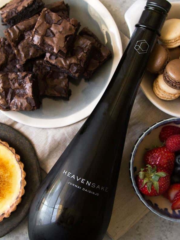 bottle of sake surrounded by creme brulee tart, brownies, macarons, and fresh berries.