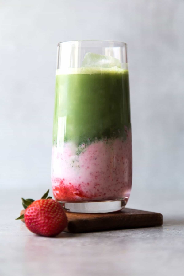 layered strawberry milk and matcha in a tall serving glass served with fresh strawberry.